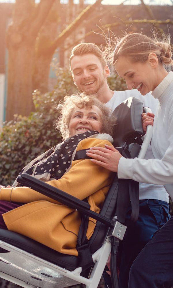 Two helpers picking up disabled senior woman in wheelchair for transport